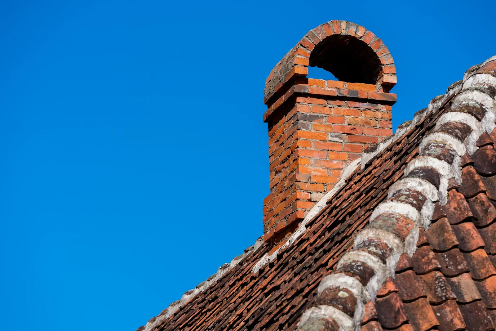Red brick chimney with an arched brick cap on a clay tile roof