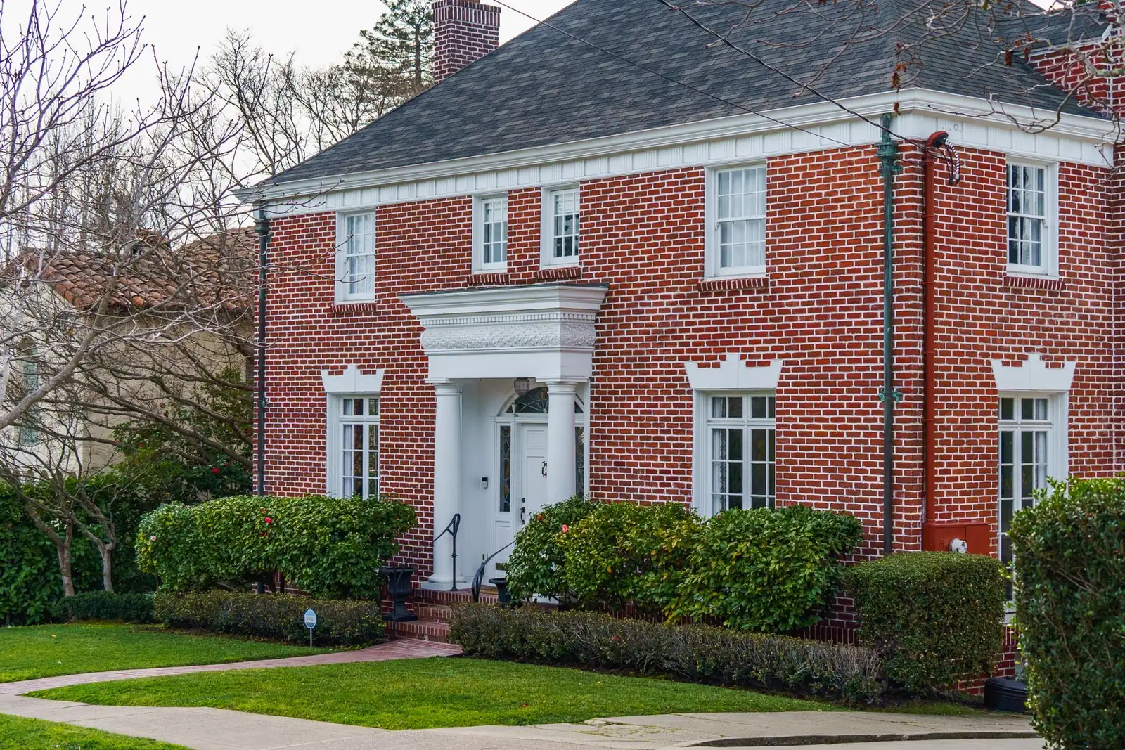 Red brick center-hall colonial with white trim, a chimney and trimmed hedges